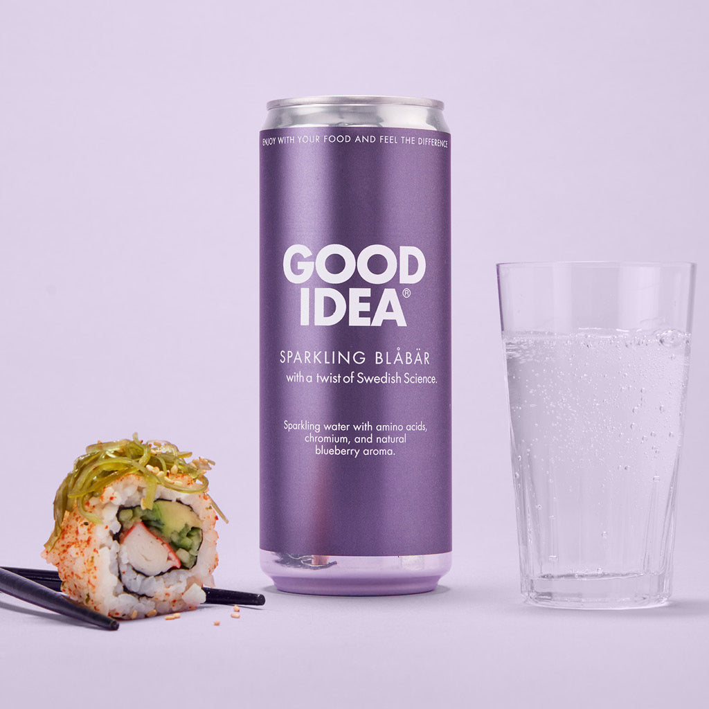Till vänster en bit sushi med ätpinnar, i mitten en burk av den blodsocker balanserande måltidsdrycken Good Idea Sparkling Blåbär, till höger ett dricksglas med bubbelvatten, mot en blå bakgrund.